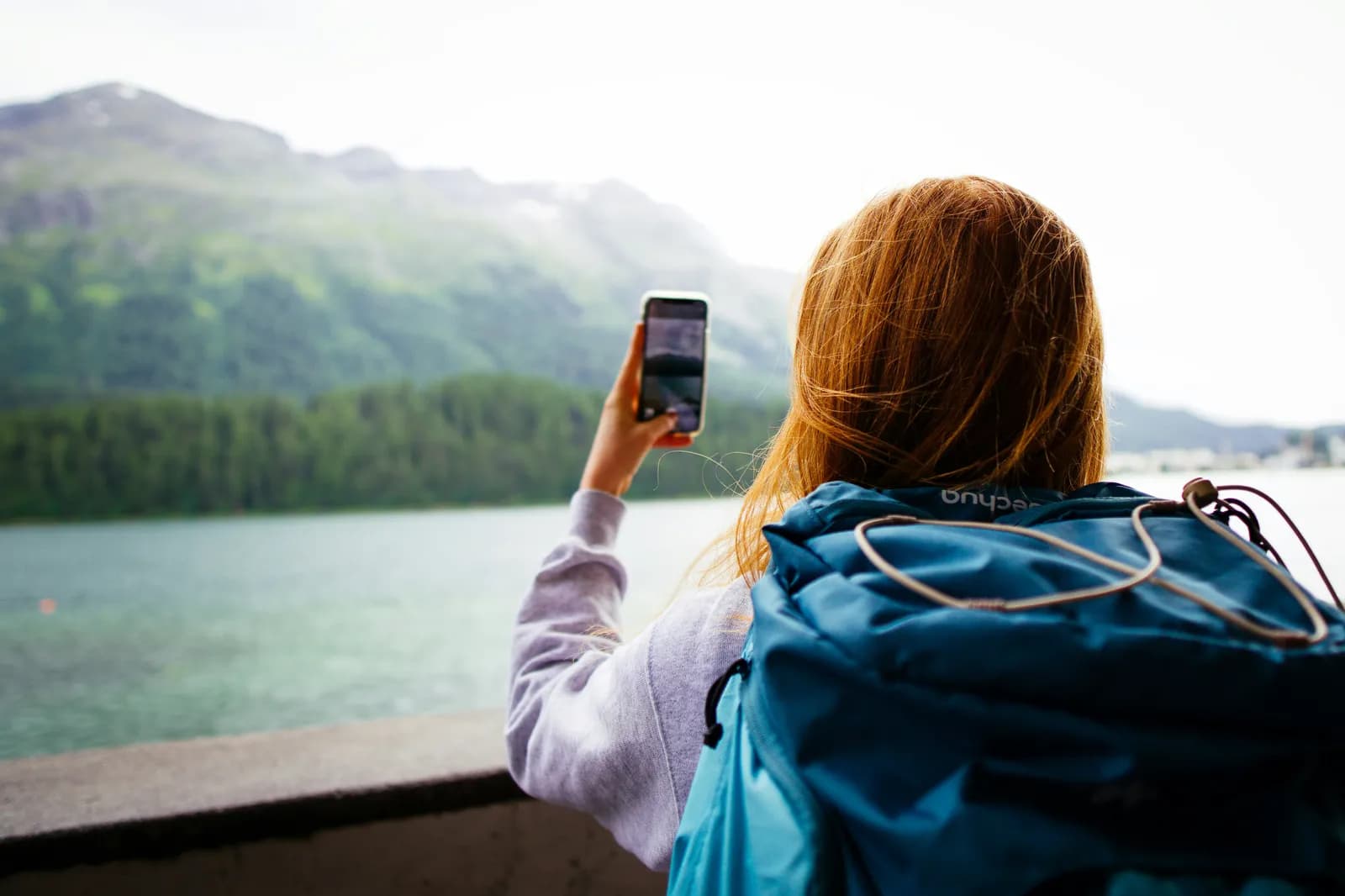Reisende macht mit ihrem Handy ein Foto an einem Bergsee im Ausland